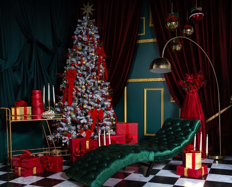 Red Muse holiday set at Hadaki Studios featuring deep red drapery, gold accents, a Christmas tree, festive gifts, and a luxe emerald chaise lounge. This is perfect for holiday photoshoots in Toronto.